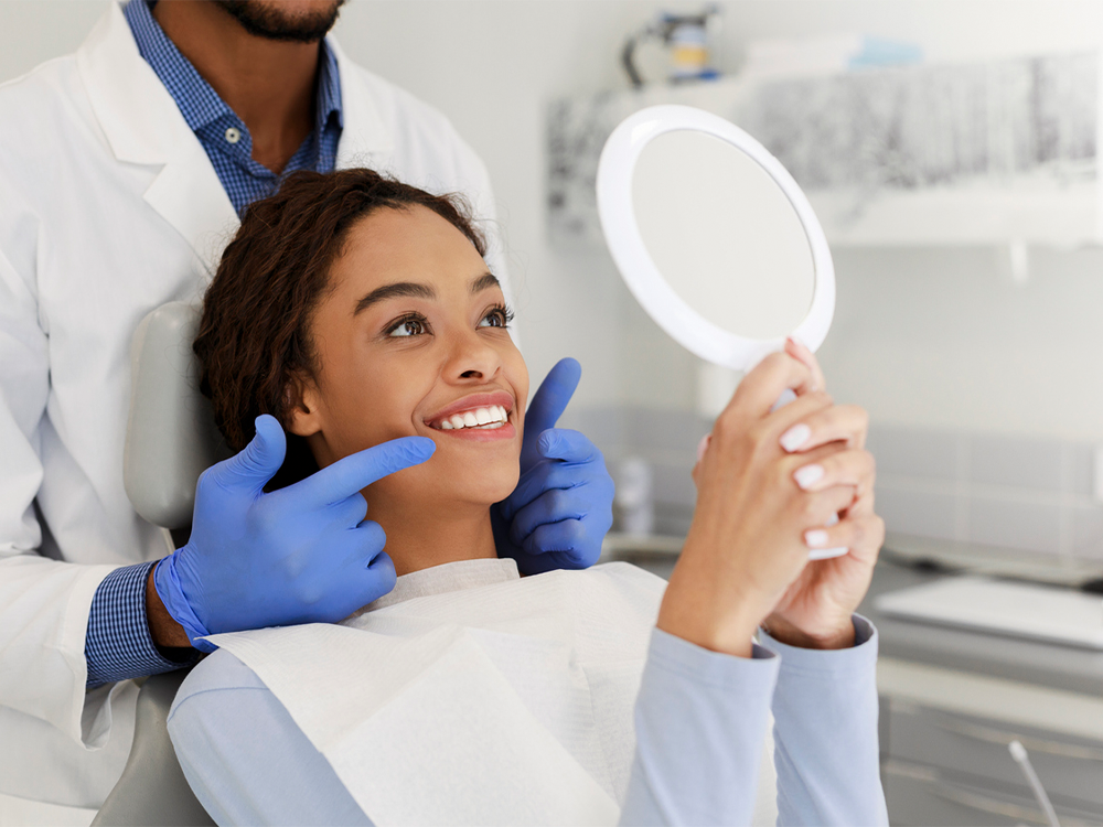 woman looking into a mirror at the dentist and smiling while the dentist points at her smile
