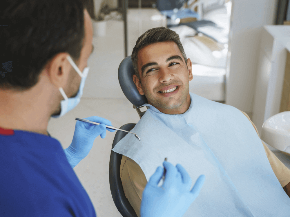 man smiling at the dentist who is holding a dental mirror